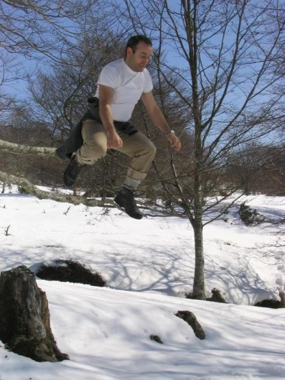 a man in white shirt jumping off snow covered slope
