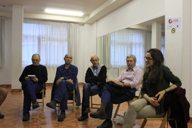 six people sitting around in chairs looking at soing