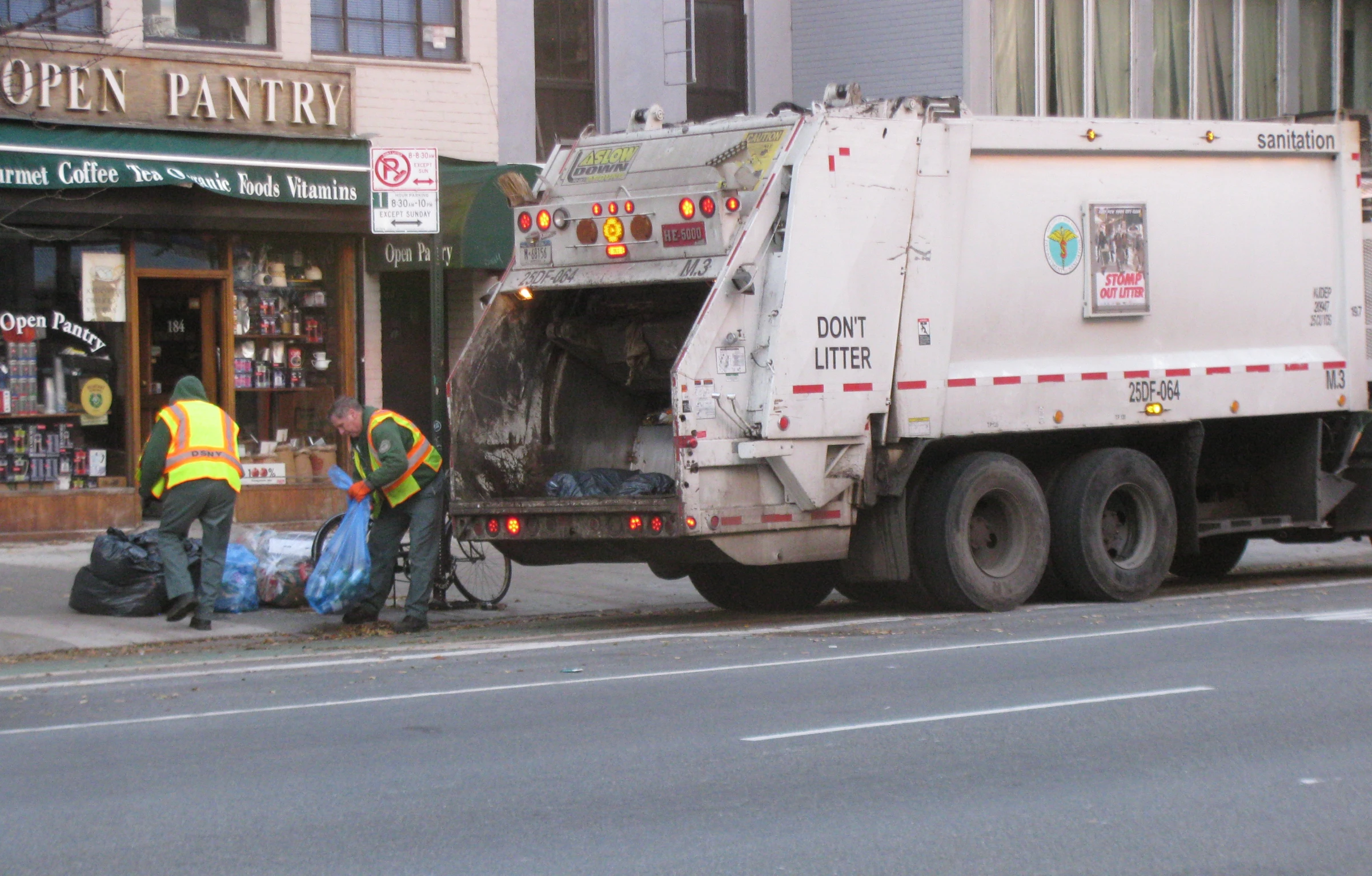 two men stand near a garbage truck while another man pulls it out