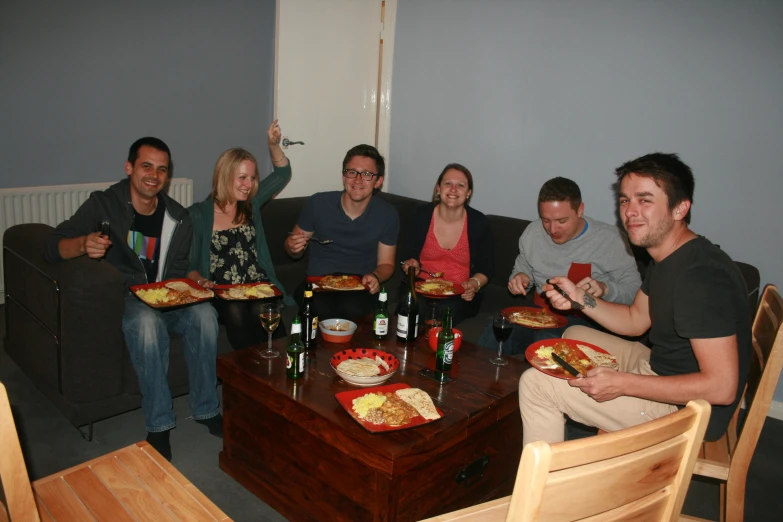 six people sitting on couches holding plates of food