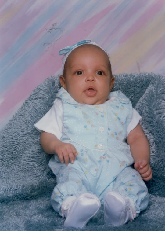 a little baby sitting in front of a gray blanket