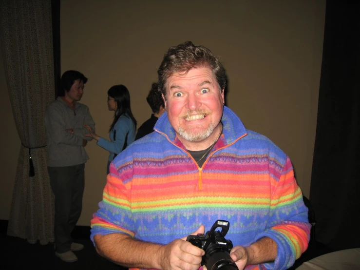 a man wearing an ugly rainbow colored shirt is holding a camera