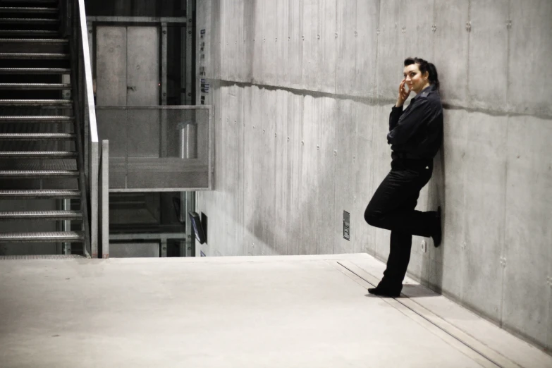 man in long black jacket leaning up against the wall