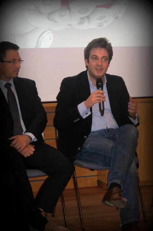 two men in suit and tie speaking in front of a crowd