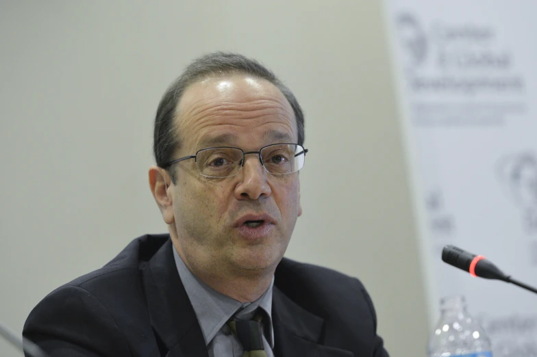 a man wearing glasses and a tie in front of microphones