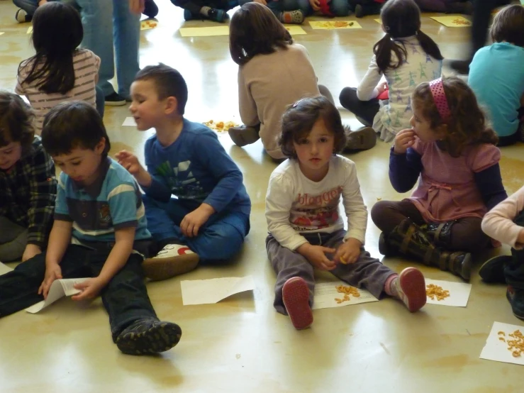 a group of children sitting on the floor eating pizza