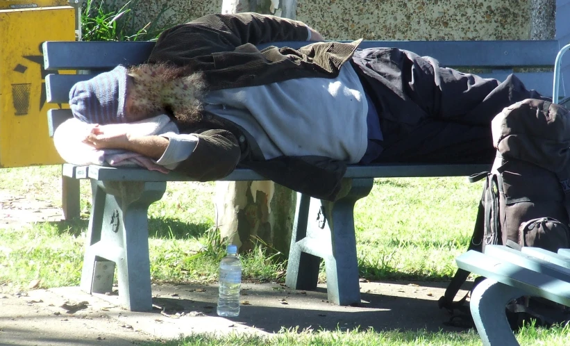 a man sleeping on a park bench in the grass