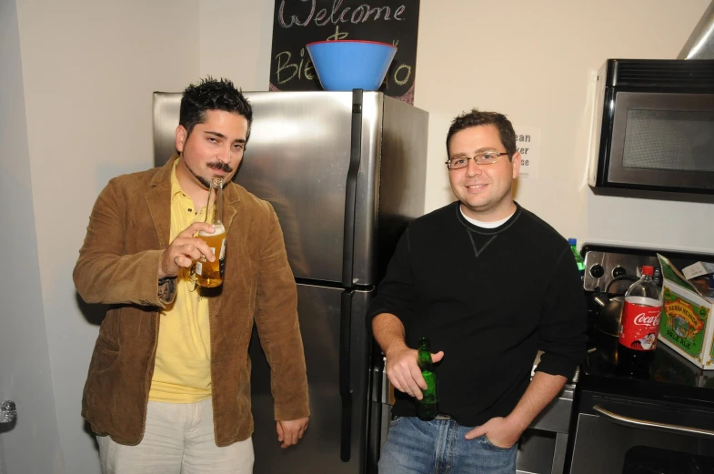 two men in the kitchen and one holding beer