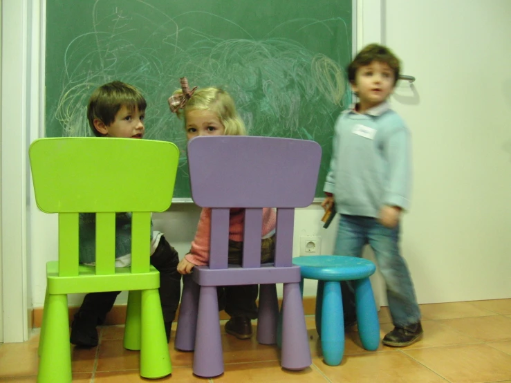 three children standing around a set of colorful chairs