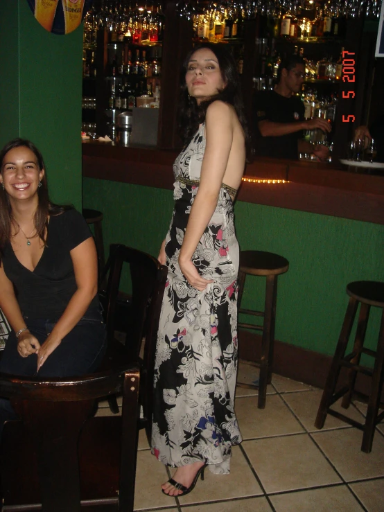 a woman stands on the side of a bar in a dress