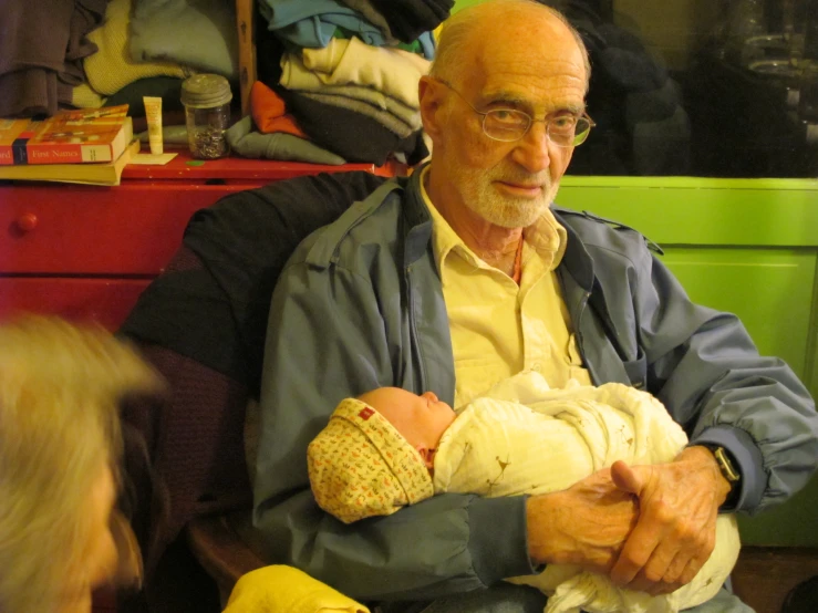 an elderly man holding a baby in his arms while another woman looks on