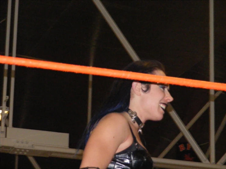 a woman in leather dress smiling with a neon orange pole on the back