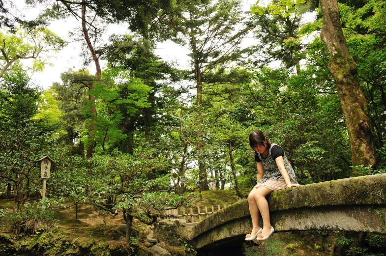 woman sitting on stone bridge in park next to water