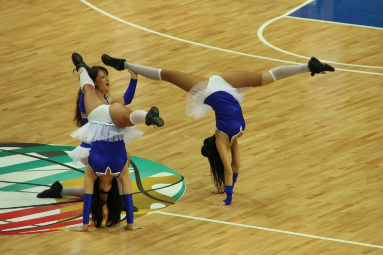 two cheerleaders doing acrobatic stunts on the court