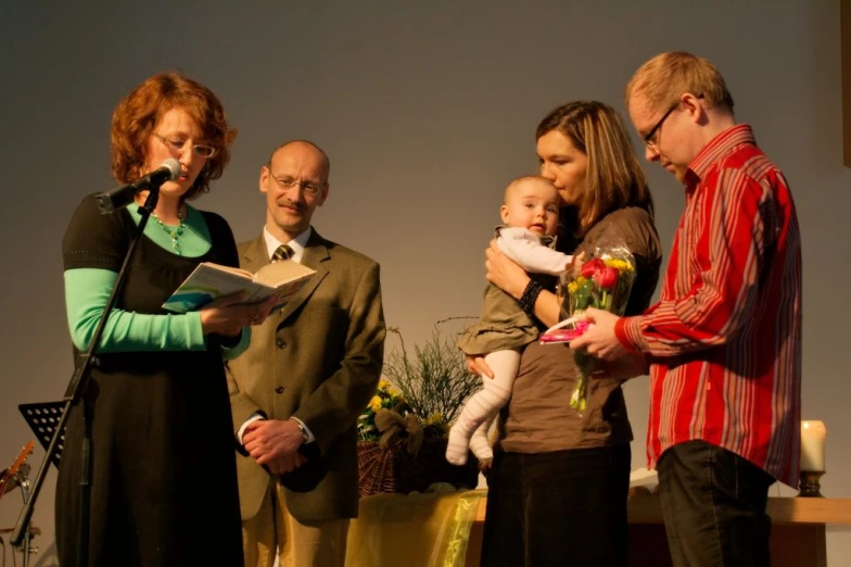 a man and woman holding a baby sing in front of a group of people