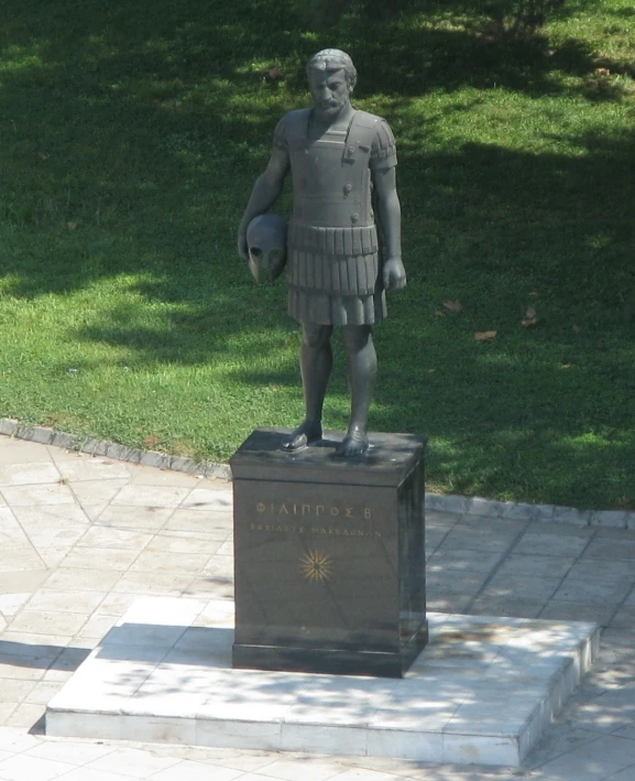 a sculpture of an ancient man stands in a grassy area