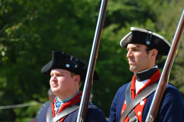 two men dressed in colonial clothing and holding red flag poles