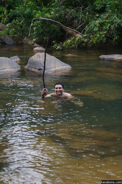 a man swimming in a river holding a large stick