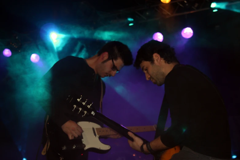 two men, one with a guitar, are standing close to each other on stage