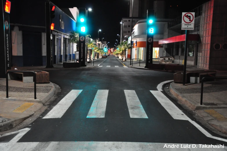 a road in the middle of a town at night with several green street lights shining