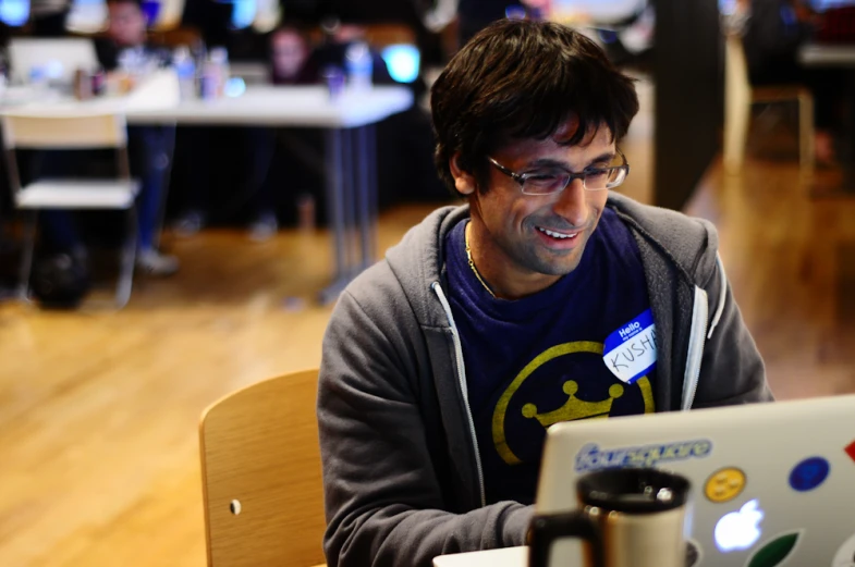 a smiling man holding onto a laptop while sitting at a table