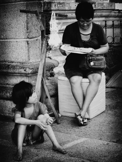 black and white po of woman reading magazine to small child sitting on the step