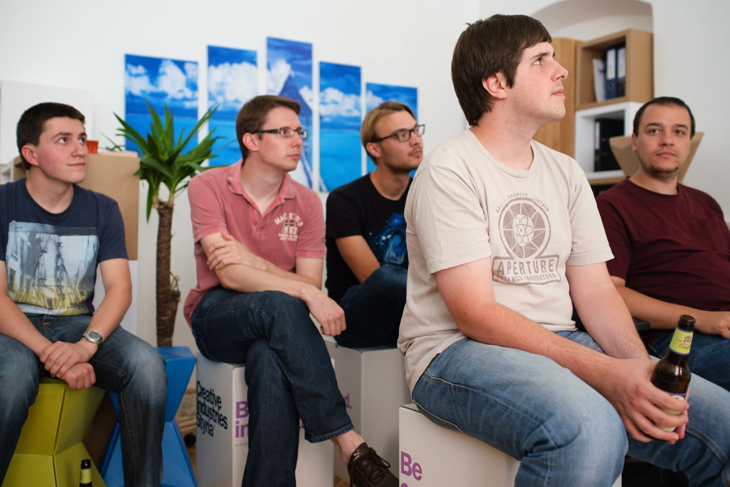 four men sitting in a waiting room with one drinking beer