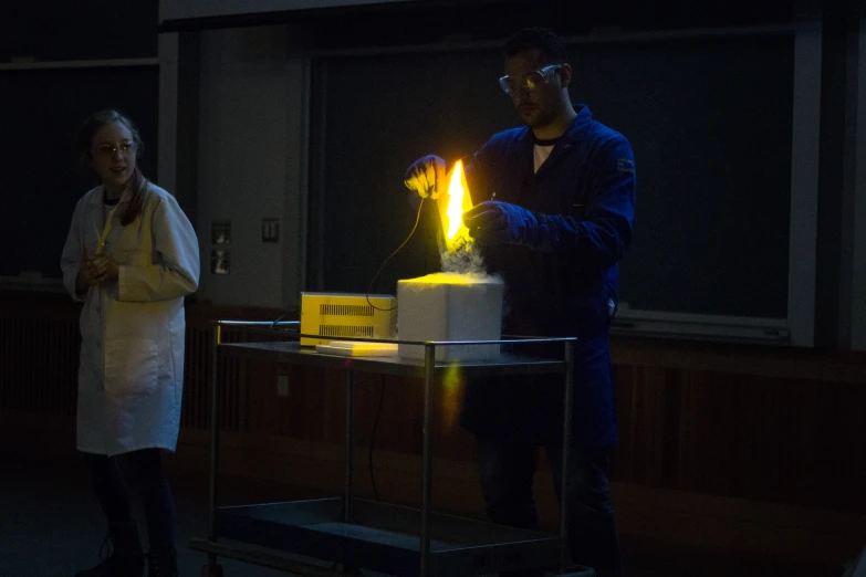 man with white lab coat standing next to a woman looking at a cake