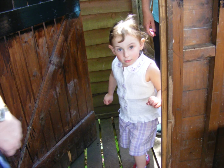 little girl in pink and purple shorts stepping out from outside house