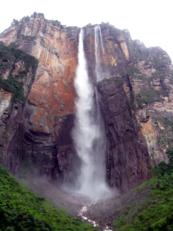 a long waterfall being held over a lush green hill