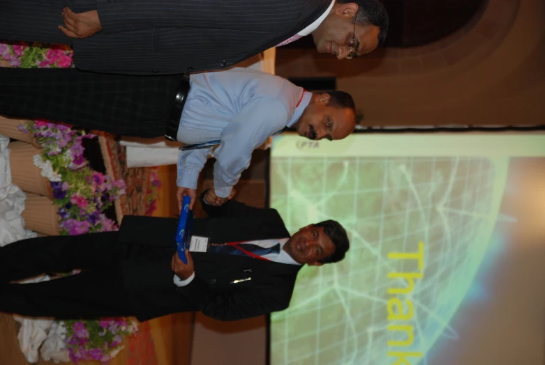 two men standing holding an award in front of a thanker board