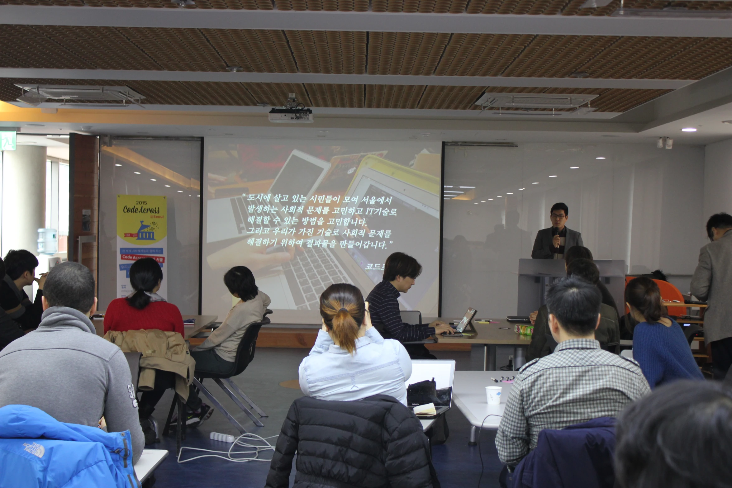 a group of people are talking in a classroom with electronic monitors