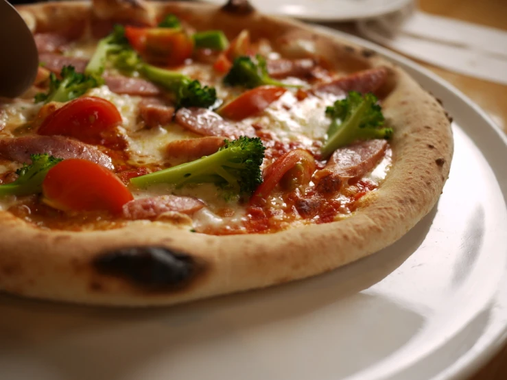 the hand of a person placing topping on a pizza