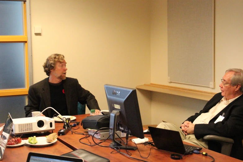 two men sitting at a table and looking at monitors