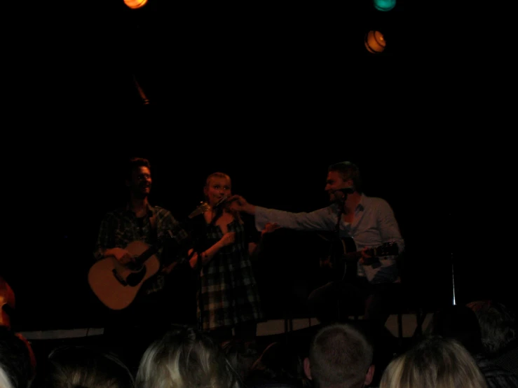 three men playing instruments while singing in front of an audience