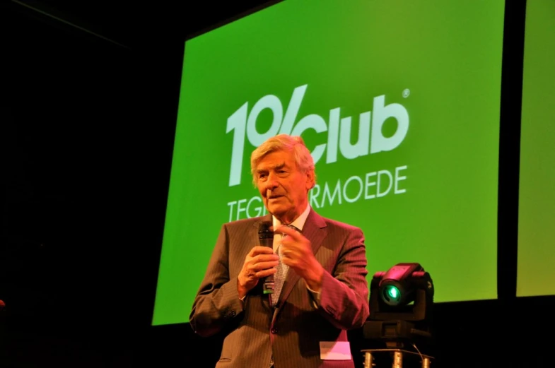 man giving a speech on stage with green and white screen