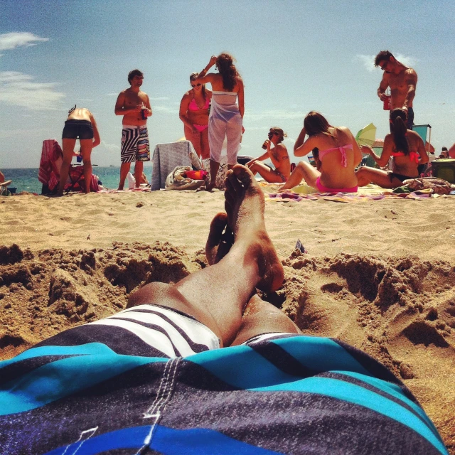 a man lying on a beach with many people in the background