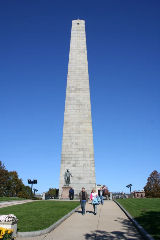 people walk down a walkway next to a very tall monument