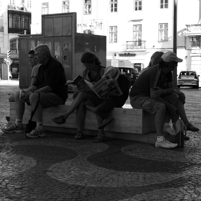 three people sitting on a bench reading magazines