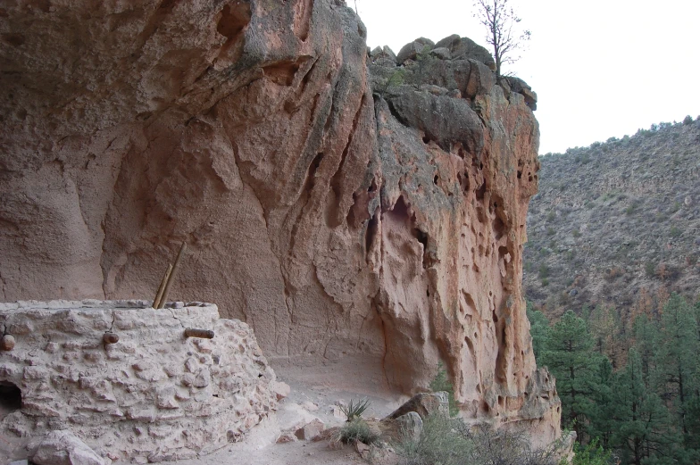 a rocky cliff next to some trees with some mountains in the background