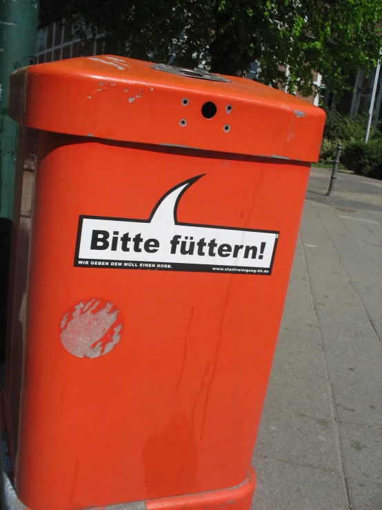 a red garbage can sitting on the side of a street