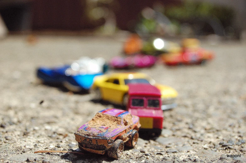 toy cars sit in a gravel road and one is small