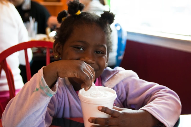 a child sitting at a table and eating a drink