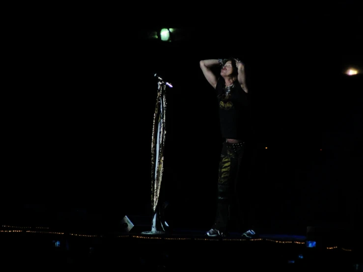 a woman wearing black standing on stage with arms behind head