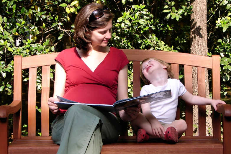 a woman sits on a park bench while reading a book to a child