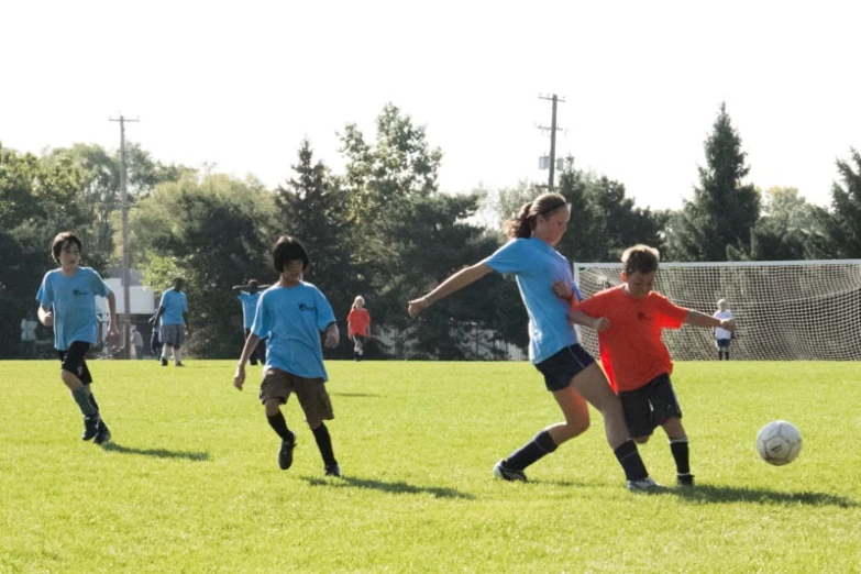 children playing soccer in the grass with trees in the background