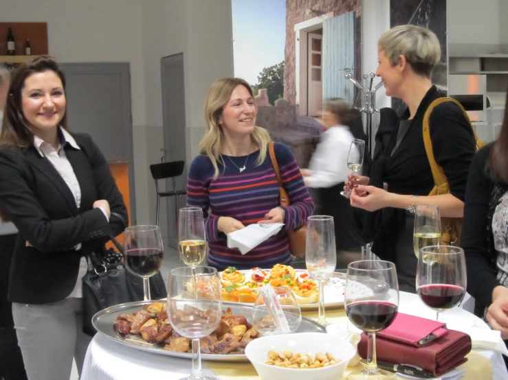 three women are standing near a round table with food