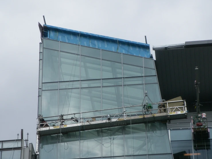 a glass building has a scaffold above it to keep construction going