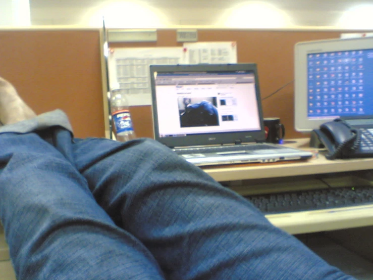 a person's legs resting on a desk with a laptop and telephone