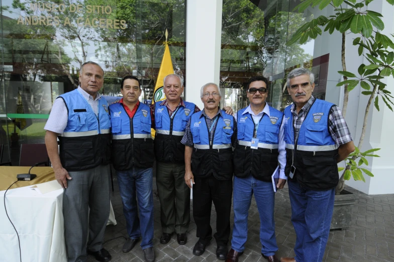 several men dressed in blue vests stand with their arms around each other